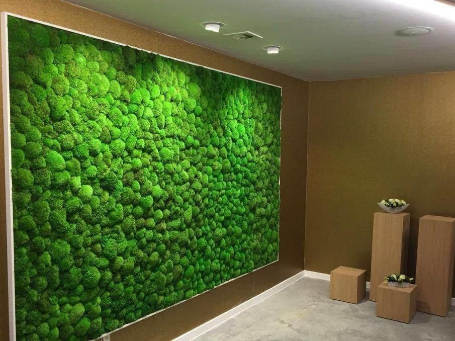 Room with a decorative green moss wall and wooden pedestal stands with small floral arrangements.